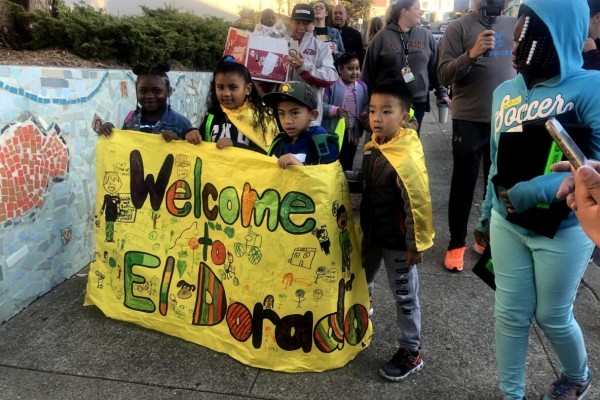 Four children hold up a yellow banner sign that reads "Welcome to El Dorado" 