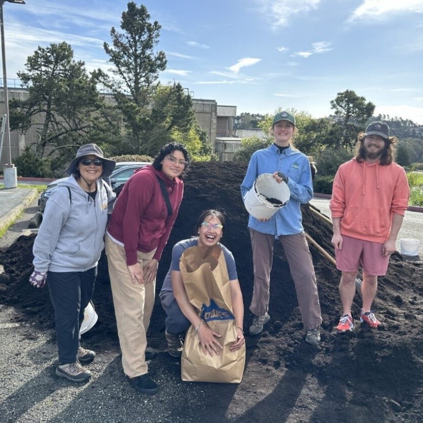 A group of five people in front of a mound of compost