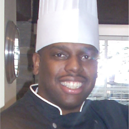man wearing white chef hat, black wardrobe smiling