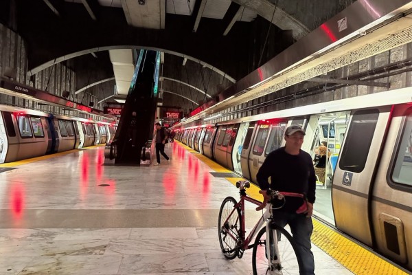 A commuter walks with his bike on the platform, next to a Bart train that is stopped at Glen Park station