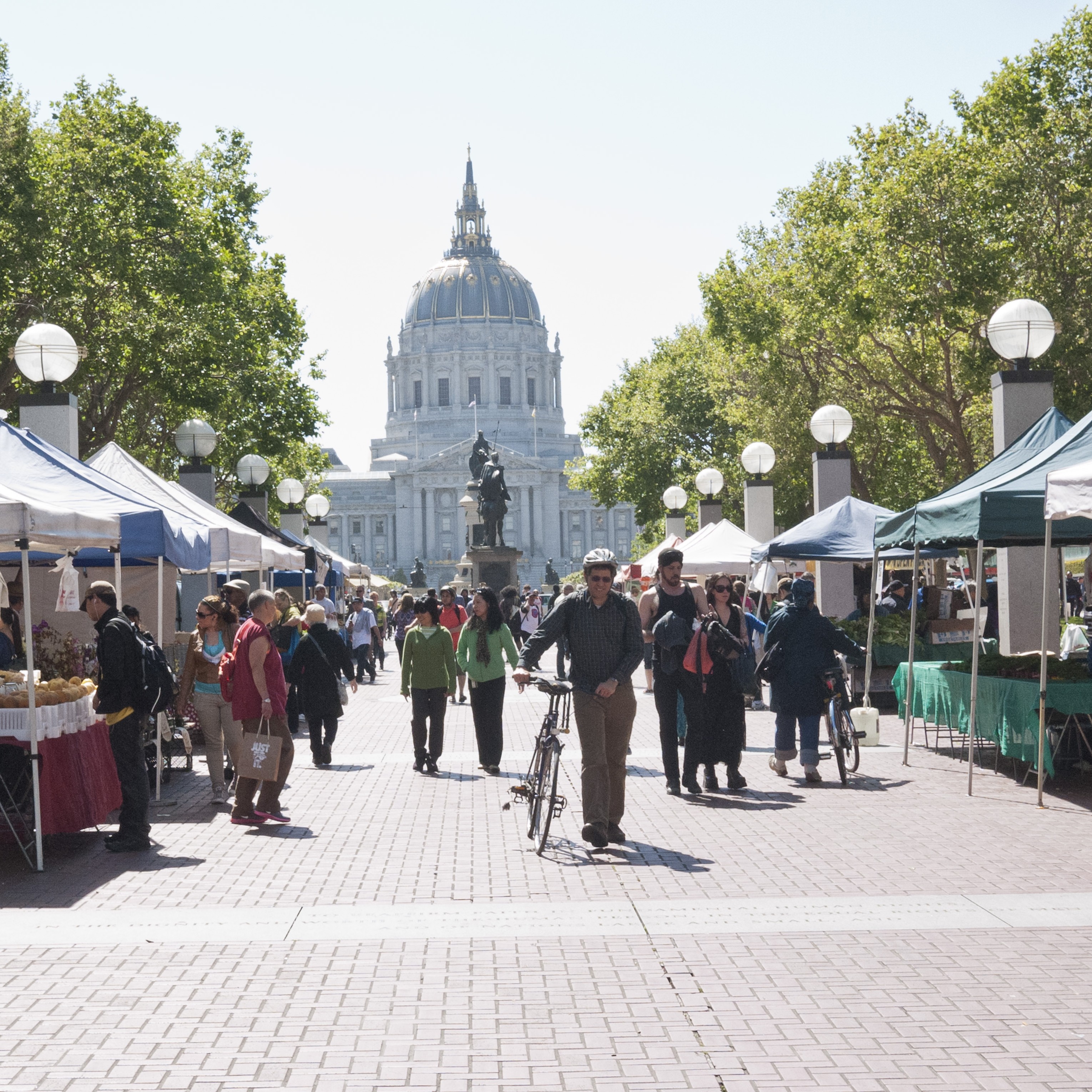 Farmers market stalls lining the street with SF City Hall in the background.